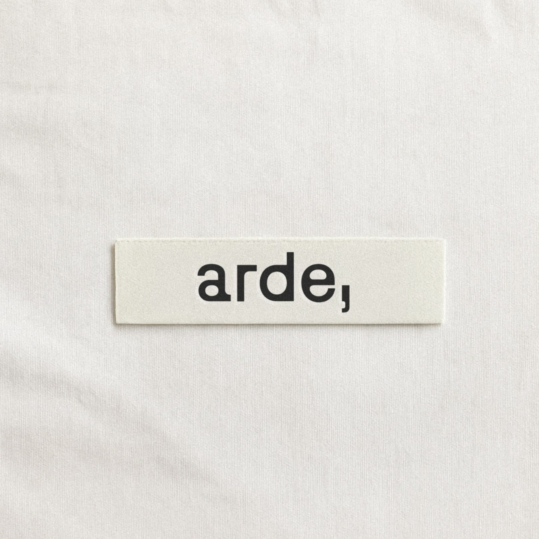 A small cream woven label printed with arde, in black, on a fabric surface.