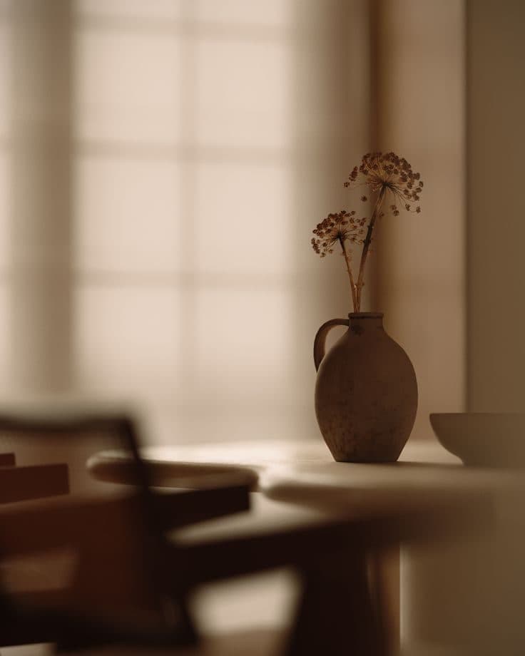A soft-focus brown interior: the back of a cane chair and a vase on a table.