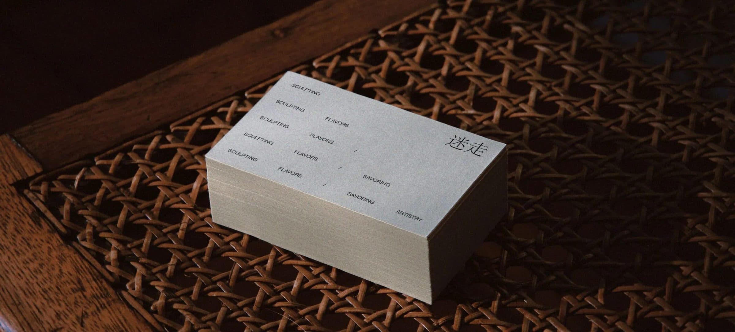 A stack of cream business cards resting on a dark, woven cane surface.