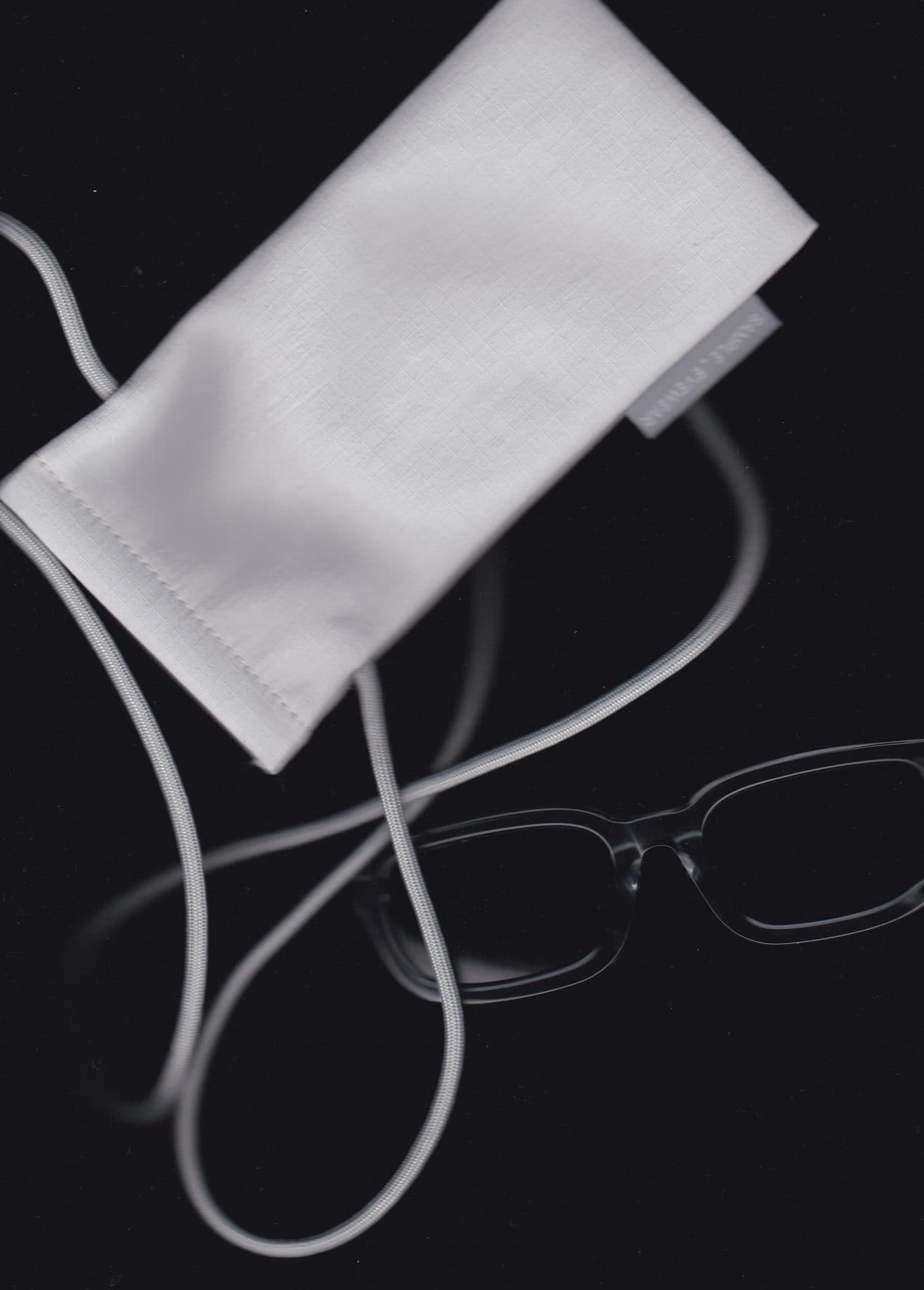 A folded white cloth pouch with a looped cord on a black ground, and a pair of clear-framed glasses lying beside it.