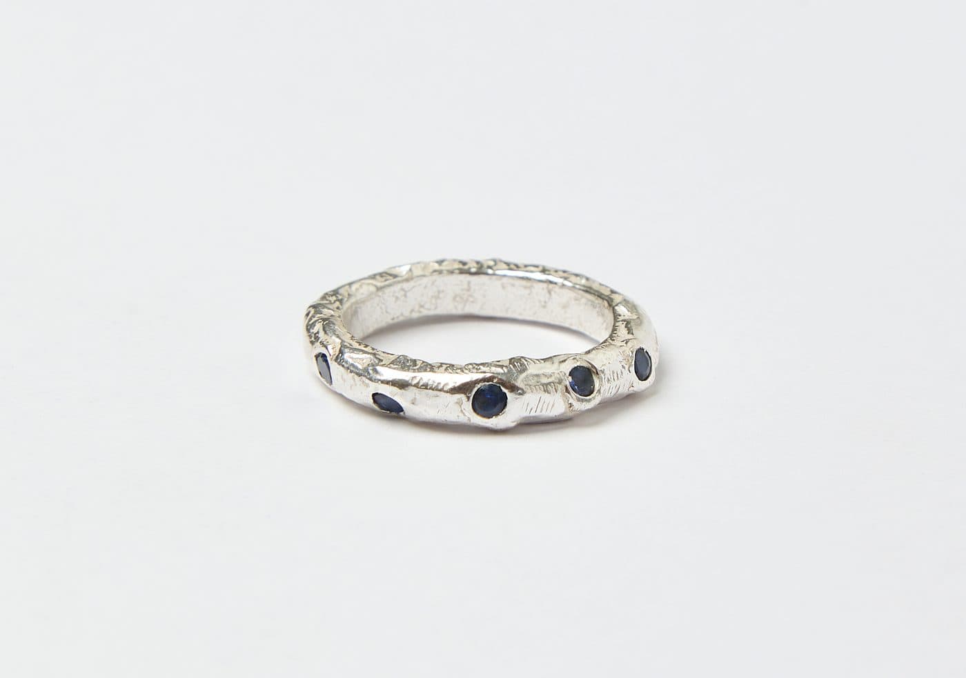 A textured silver ring set with dark stones, on a pale grey ground.