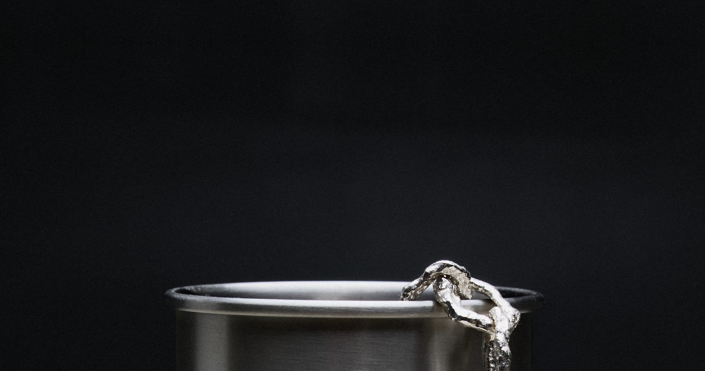 The rim of a steel canister on a black ground, with a chunky textured silver chain draped over its edge.
