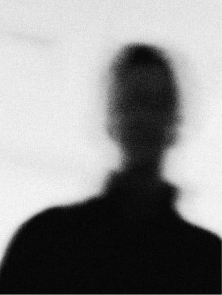 Blurred black silhouette of a head and shoulders on a grey field.