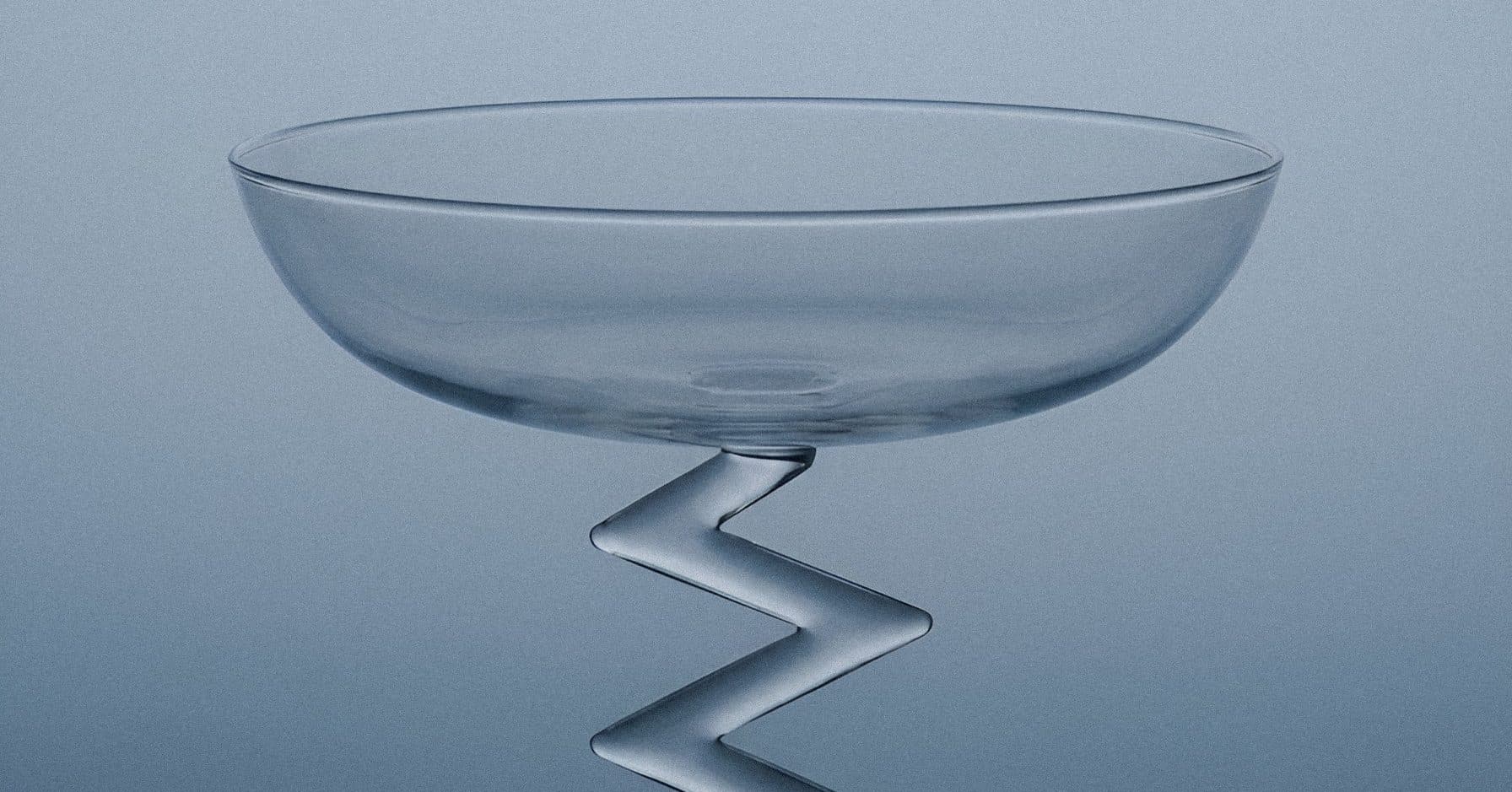 A clear glass compote with a zigzag stem, lit against a deep blue gradient.