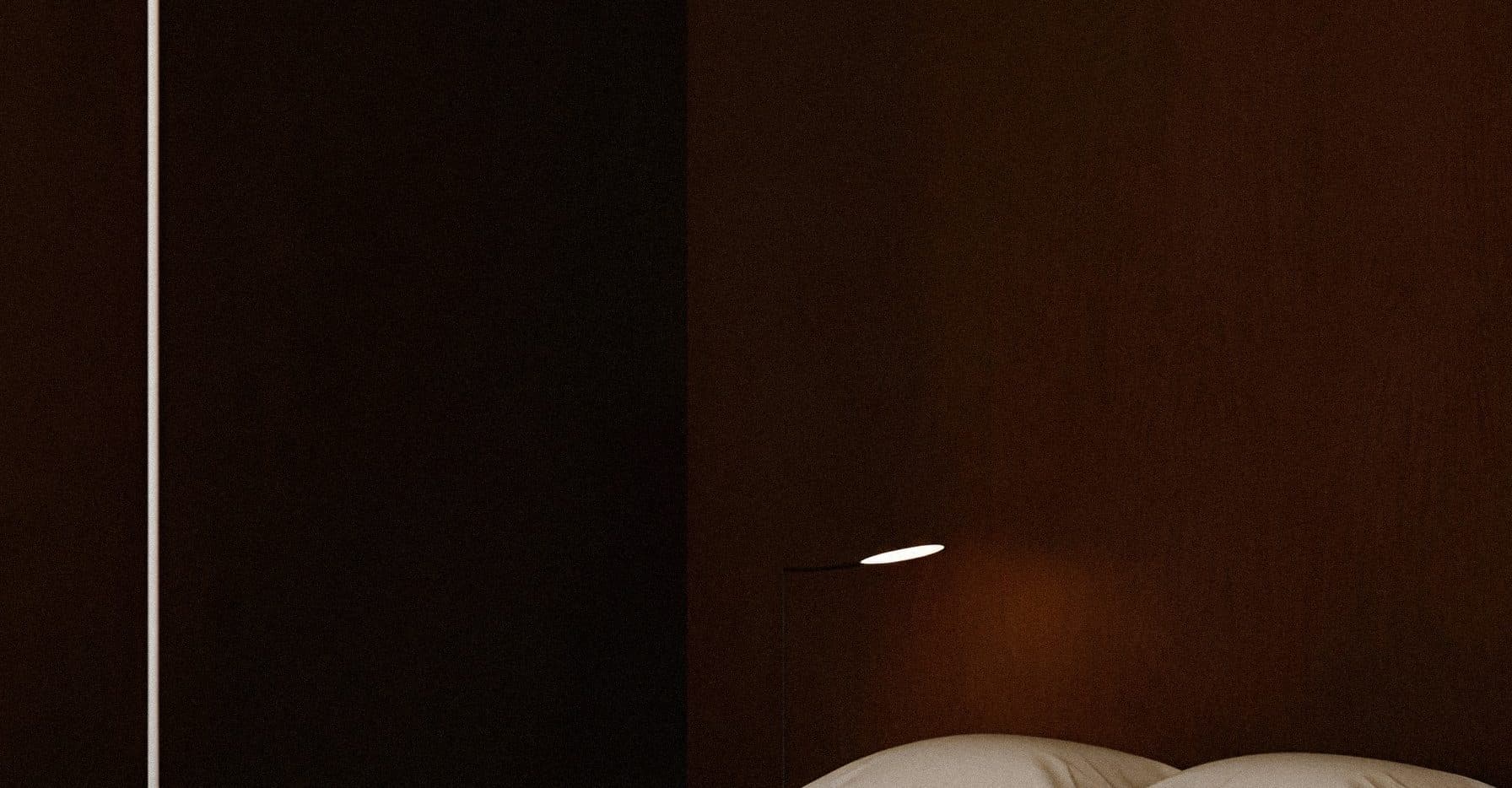 A dark timber-panelled bedroom wall with a tall floor lamp at the left, a small reading lamp and the tops of two pillows along the bottom edge.