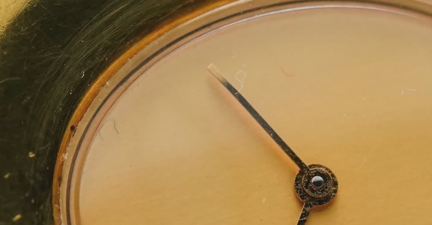 Close-up of a brass wristwatch dial with two thin black hands.