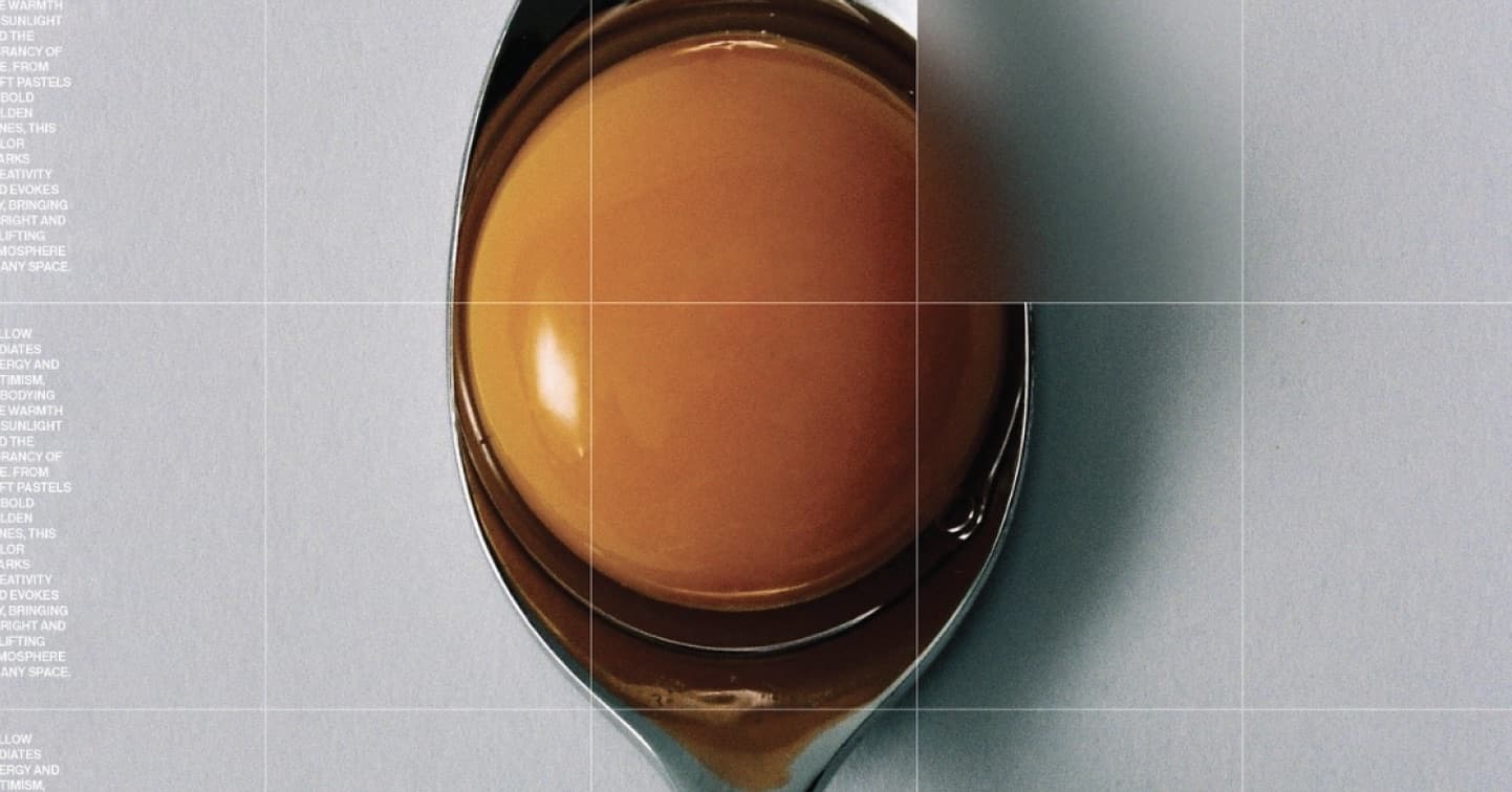 Top view of a steel spoon holding an amber egg yolk on a pale blue-grey surface.