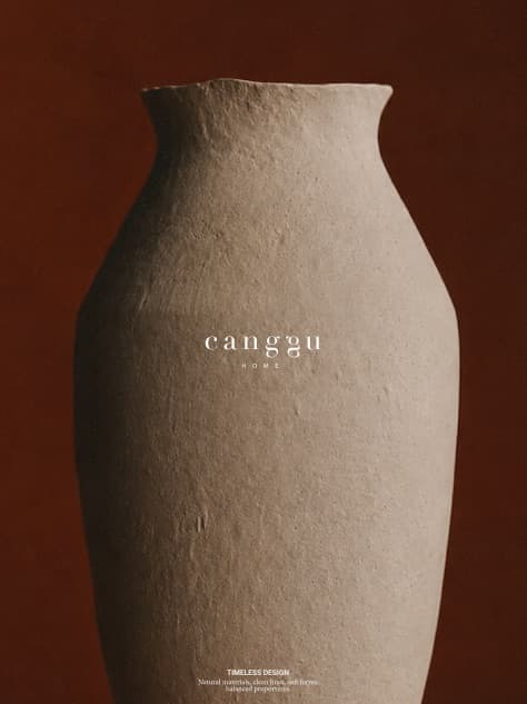 A tall hand-formed ceramic vase in beige clay against a deep brown-red wall, with the brand name Canggu Home in small type.