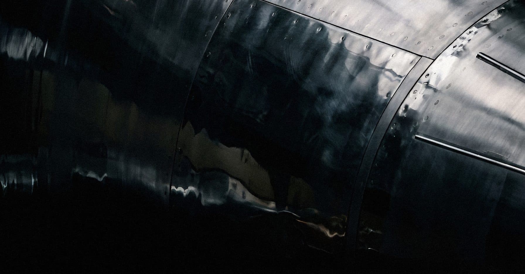 Dark, polished aluminium fuselage panels with rows of rivets and soft reflections fading into black.