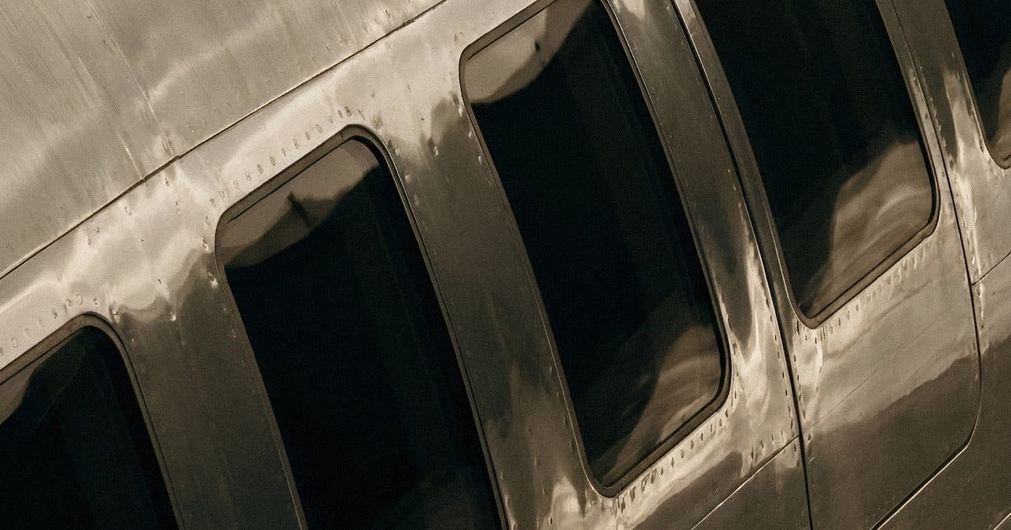 A row of dark cockpit windows set into a worn, polished aluminium fuselage.