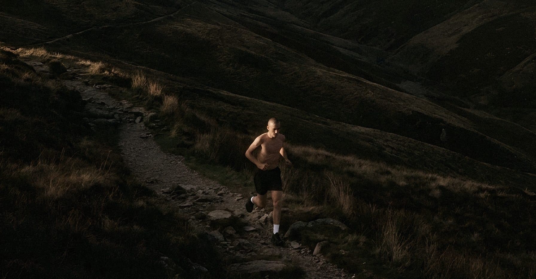 A lone runner on a narrow trail across dark hills at dusk.